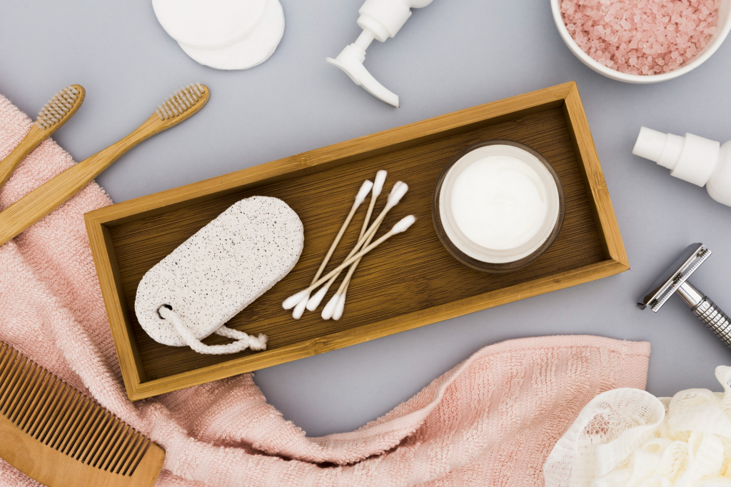 An aesthetic flat lay of essential beauty and personal care products on a bamboo tray, including wooden toothbrushes, cotton buds, skin cream, and a comb for a natural skincare routine
