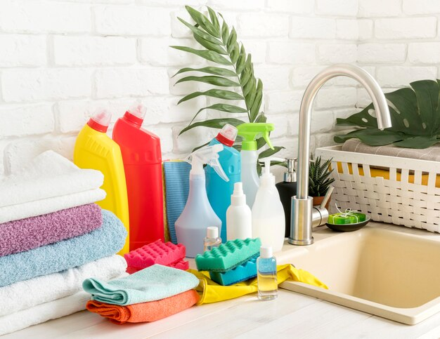 A variety of household cleaning products, eco-friendly supplies, and colorful sponges arranged neatly by a kitchen sink for effective home hygiene and surface care.