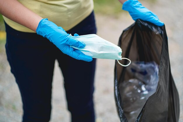 A healthcare worker in blue nitrile gloves disposing of a used face mask into a black cytotoxic waste bag, highlighting the importance of proper medical waste labelling and safety