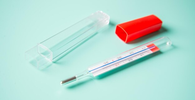 A glass clinical thermometer shown with its protective plastic sheath cover and red cap to demonstrate hygiene and storage safety.