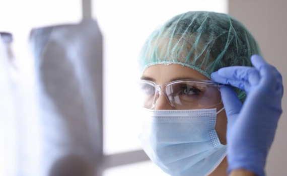 A female healthcare professional wearing clear protective eyewear, a surgical mask, and a bouffant cap to ensure workplace safety and eye protection.