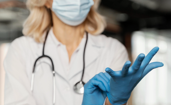 Doctor with medical mask putting on medical gloves