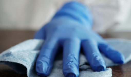 Hospitality worker wearing gloves disinfecting a table with a cleaning wipe