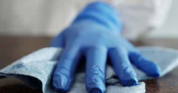 Hospitality worker wearing gloves disinfecting a table with a cleaning wipe