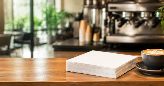 A clean café counter with neatly folded white lunch napkins beside a coffee cup and cutlery