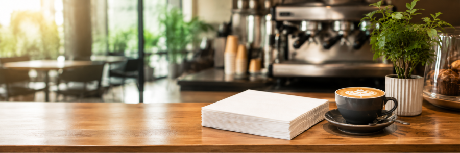 A clean café counter with neatly folded white lunch napkins beside a coffee cup and cutlery