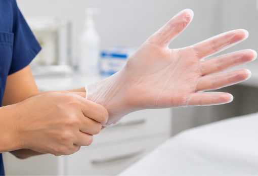 Close-up of a healthcare worker's hands putting on clear vinyl examination gloves before a patient consultation