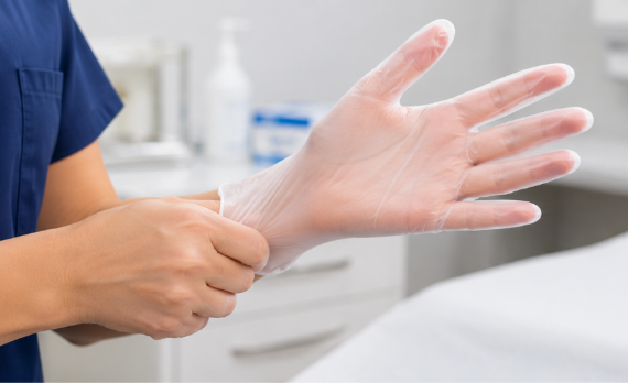 Close-up of a healthcare worker's hands putting on clear vinyl examination gloves before a patient consultation