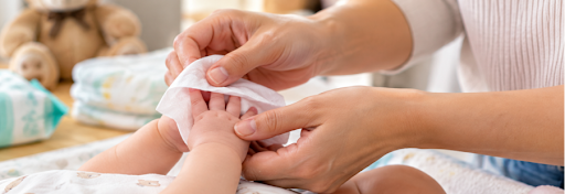 Parent's hands using a baby wipe to clean an infant's hands during a nappy change